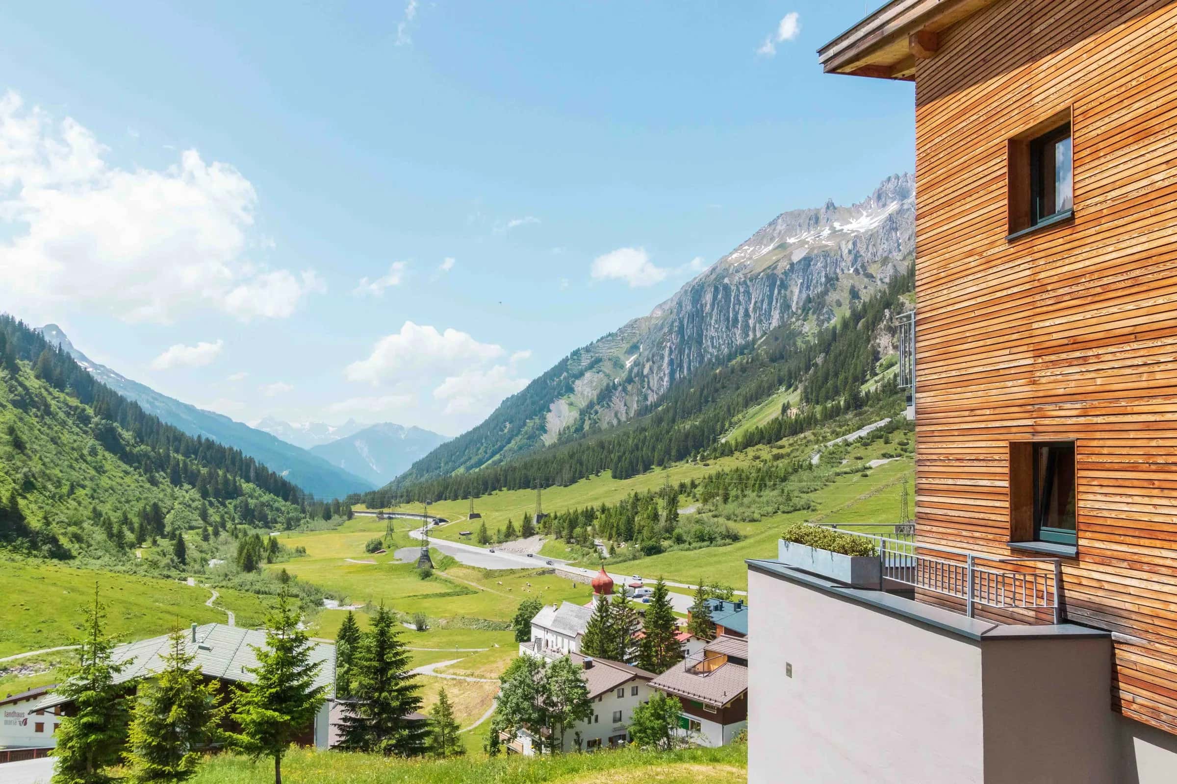 Hotel mit Holzfassade und Balkon über einem grünen Alpental