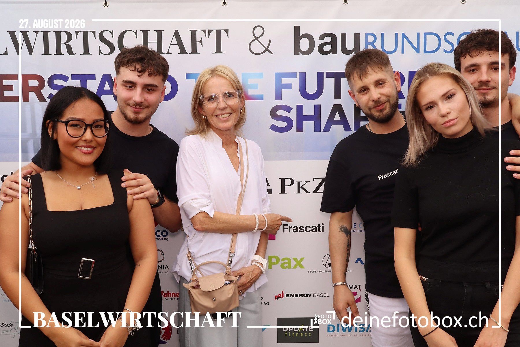 Sechs Gaeste des Networking Events vor der Fotowand, darunter drei Mitarbeiter von Frascati in schwarzen Firmenshirts