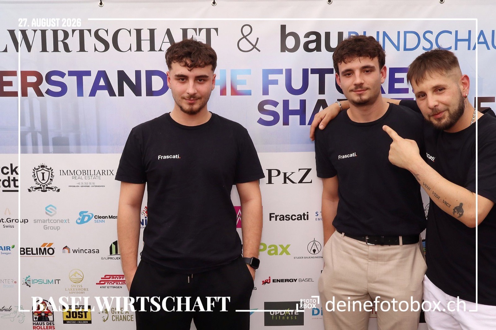Drei Mitarbeiter von Frascati in schwarzen Firmenshirts vor der Fotowand mit den Logos der Partner